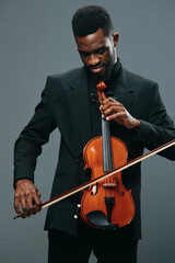 Elegant African American man in tuxedo holding violin against a gray background, classical music...