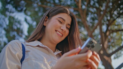 Cheerful student texting smartphone in sunny park. Closeup woman laughing mobile