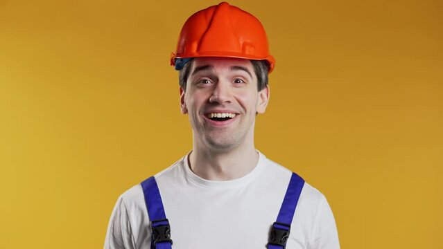 Shocked industrial specialist worker in helmet man glad, he screaming WOW. Impressed guy trying to get attention on yellow background.