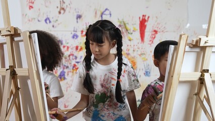Playful student painted or draw canvas at stained wall with diverse friends in art lesson. Group of...