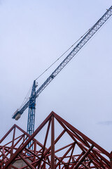 Fototapeta na wymiar Geometric composition of red metal beams and a blue crane in a modern construction against a clear sky.
