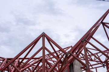 Geometric composition of red metal beams and a blue crane in a modern construction against a clear sky. - obrazy, fototapety, plakaty