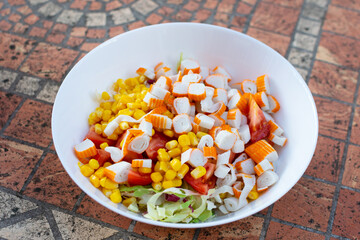 Featuring crab sticks, sweet corn, and green lettuce, a colorful salad is elegantly served on a...