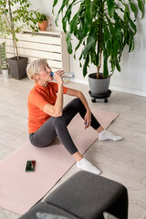 Beautiful senior woman drinking water after exercise. Active senior woman practicing yoga indoors. Exercise for Older Adults