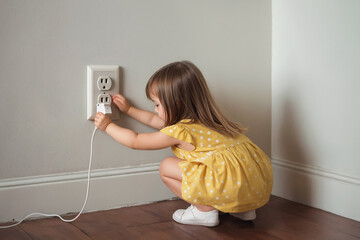 Little girl touches charging unit with wire and plays with electrical outlet in wall