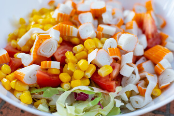Multi-colored appetizing salad with crab sticks, corn and green lettuce in a white plate, close-up