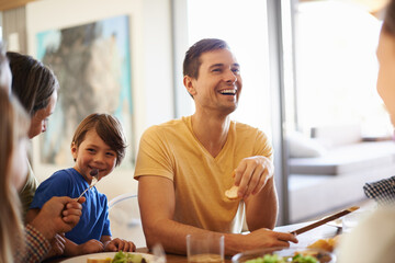 Family, together and eating food in house for nutrition with dining table, talking and tableware. Young boy, happy people and hosting for lunch with conversation, salad and smile in home for laughing