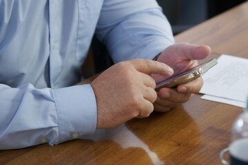 An adult male businessman in a light blue shirt is using a cell phone - smartphone while sitting at...