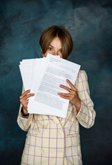 Fototapeta premium portrait of romantic smiling beautiful woman in white jacket staying on dark blue background and holding manuscripts in her hands. writer. Teacher. Education conception