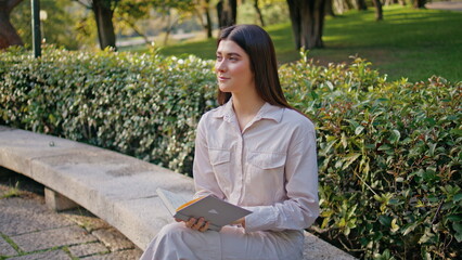 Romantic girl reading book in green park. Relaxed student study sitting bench
