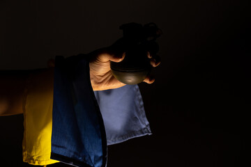 A hand grenade in the hands of a girl in the dark and the flag of Ukraine, a combat grenade, help