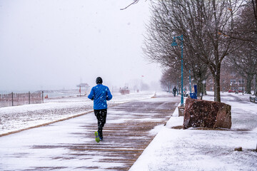 winter running: a jogger runs away from the camera on an empty wooden boardwalk beside a snow swept...