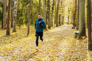 A joyful jogger in a teal jacket savors a crisp autumn run amid a golden-hued forest pathway.