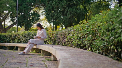 Relaxed reader sitting park bench reading book. Girl answering smartphone call
