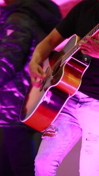 vertical video, young latino male musician playing corridos tumbados on an acoustic guitar. Mexican music concert