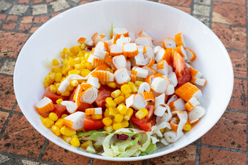 Served on a white plate, a tantalizing salad incorporates crab sticks, corn, and leafy green lettuce, boasting vibrant colors