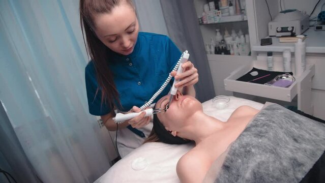 Beautician cosmetologist performs a facial procedure using a microcurrent therapy device in the area around the eyes. Hardware cosmetology in the clinic salon for a client