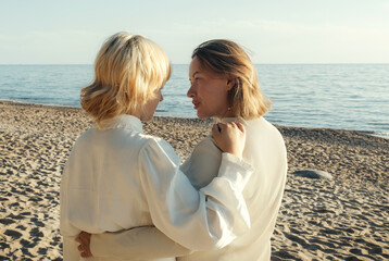 Mom and daughter are standing on the beach by the sea, hugging