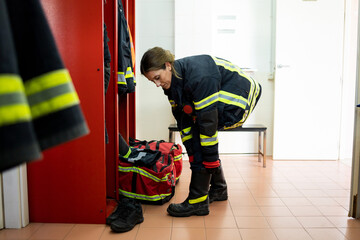 An adult Caucasian woman works as a firefighter dressed in uniform.The senior woman is in the locker room putting on her boots to go to an emergency.Concept of women in risky professions.