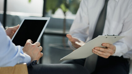 businessman holding tablet, male colleague nearby holding contract