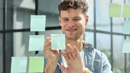 business man standing in front of stickers glass wall and write task on sticker at his office place