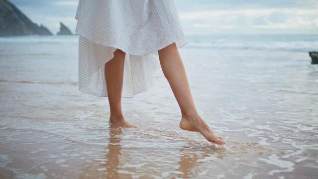 Girl legs going waves beach closeup. Relaxed female traveler walking ocean coast