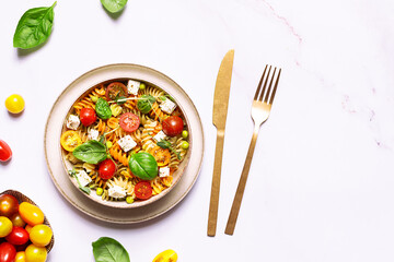 Colorful full grain fusilli pasta warm salad with feta cheese, cherry tomatoes, herbs, green pea...