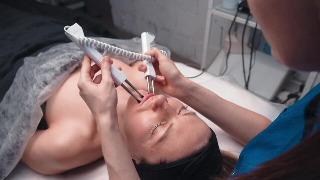 Beautician cosmetologist performs a facial procedure using a microcurrent therapy device in the area around the eyes. Hardware cosmetology in the clinic salon for a client