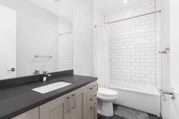 A bathroom with a brown cabinet, black marble countertop, and a white subway tile shower.