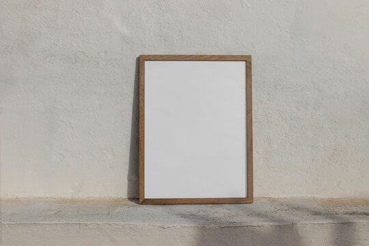 Minimal empty vertical wooden frame picture mockup against white old textured white wall in sunlight. A4, A3, A2 poster template. Neutral Summer background with light, shadows. Mediterranean design.
