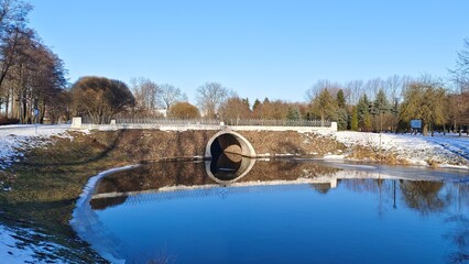 The water channel in the city park flows under the bridge and is partially covered with ice in...