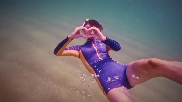 Girl scuba diver makes a heart or sign of love underwater. Young athletic woman shows heart gesture with hands while having a blast in the sea