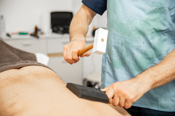Masseur nutzt einen therapeutischen Hammer zur Massage /  Masseur uses a therapeutic hammer for...