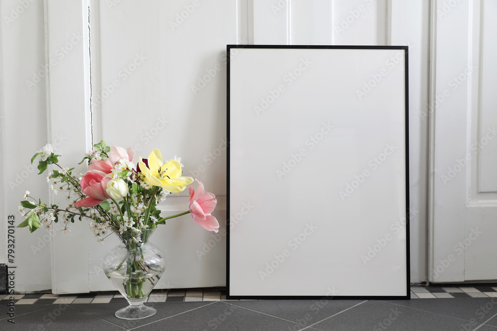 Wall mural spring still life scene. tulips, cherry tree blossoms bouquet in glass vase. blank black picture fra