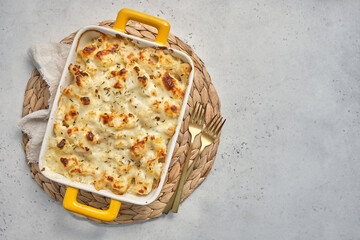 A cheesy macaroni and cheese cauliflower casserole in a yellow handled dish