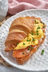 A croissant sandwich with eggs and salmon on a white plate