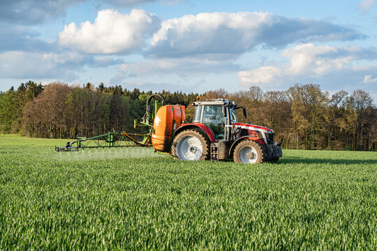 Getreideanbau - roter Traktor mit angebauter Feldspritze bei einer Pflanzenschutzma&szlig;nahme im Getreidefeld.