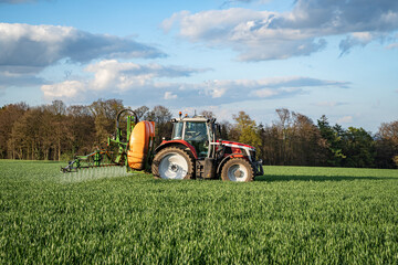 Getreideanbau - roter Traktor mit angebauter Feldspritze bei einer Pflanzenschutzmaßnahme im...