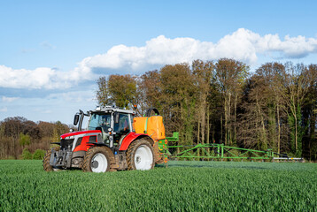 Pflanzenschutz im Ackerbau - roter Traktor mit Feldspritze im Getreidefeld, Frontansicht.