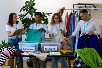 Group of volunteers, young women and man, sorting clothes in charitable foundation for charity...