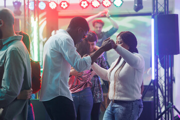 Young man and woman friends holding hands while dancing at nightclub party. African american couple...
