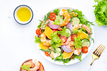 Fresh delicious shrimp salad with orange, lettuce, tomatoes, cucumbers, onions and sesame seeds with olive oil, white background, top view