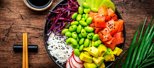 Poke bowl for balanced diet with salmon, avocado, radish, cabbage, beans, sesame and rice, wooden table background, top view banner close-up