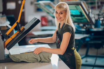 Portrait of smiling female print shop worker using heat press on tee.