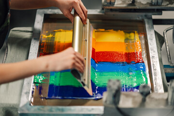 Close up of graphic worker's hands screen printing with squeegee.