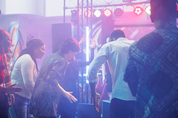 Cheerful clubbers laughing while improvising dance battle at discotheque in nightclub. Carefree man and woman friends showing moves on dancefloor while having fun at club party