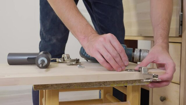 Carpenter man drilling round holes in a wooden chipboard plate for door hinge. Door furniture. Woodworking industry and furniture assembly concept 