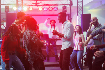 Young friends group partying on dancefloor and improvising dance battle in nightclub. Diverse...