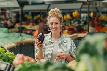 Portrait of smiling shopper woman buying eggplant at farmers market.