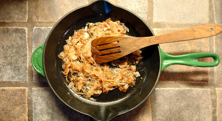 caramelized onions in an enameled cast iron frying pan with an olive wood spatula on a porcelain...